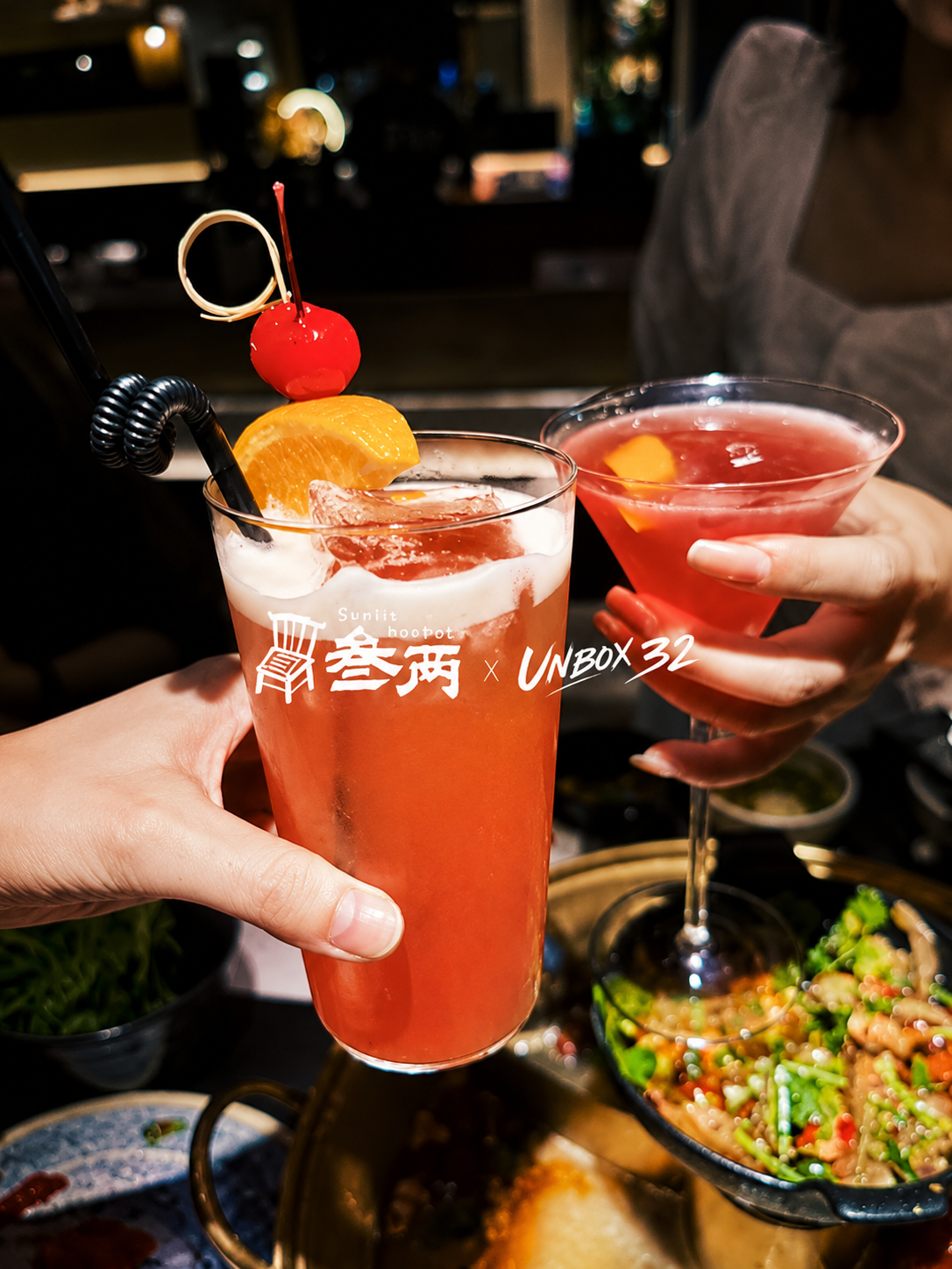 Two guests holding SUNLIT HOTPOT cocktails over a table